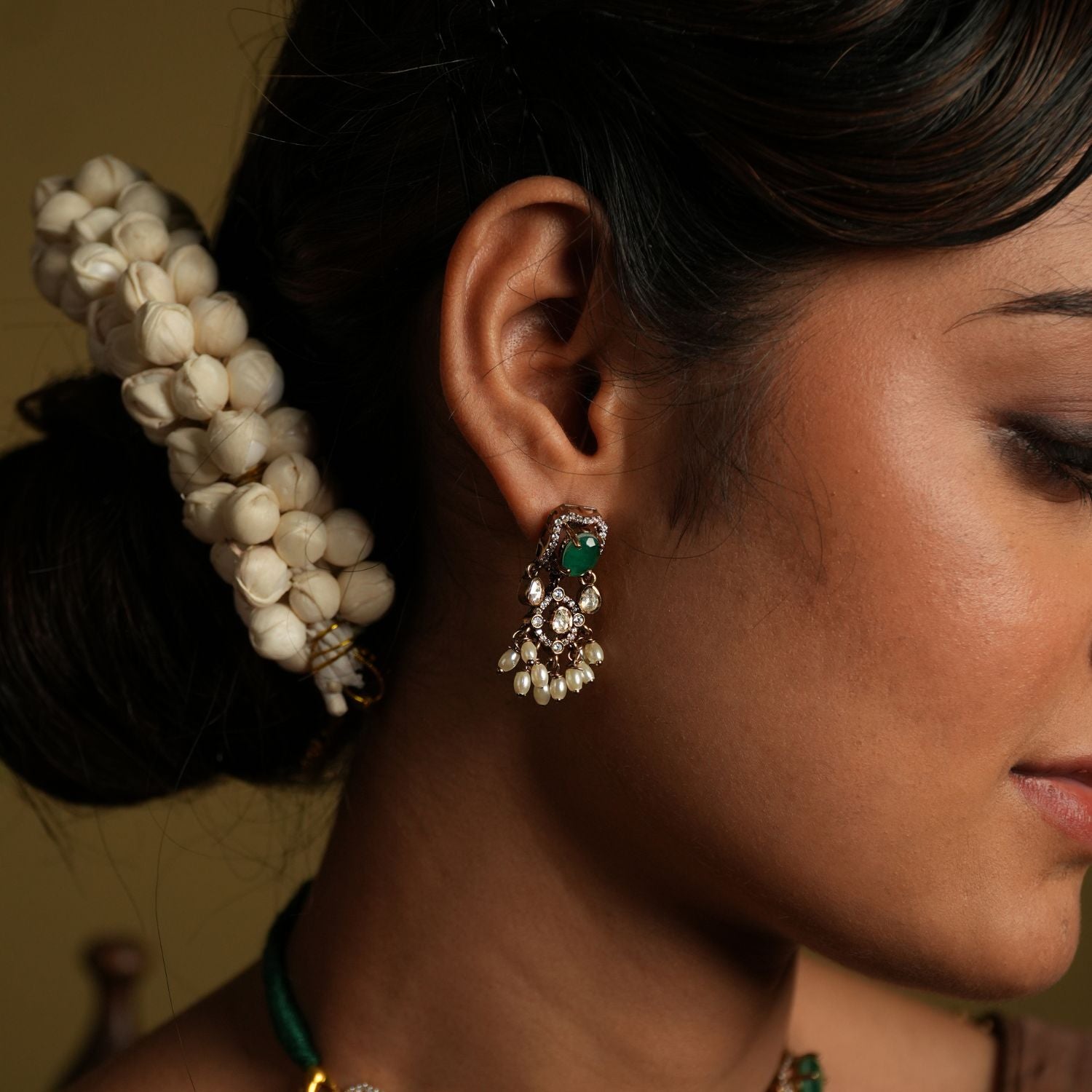 Enhance your traditional look with this exquisite silver gold-plated jewelry set featuring a stunning pair of earrings and a matching necklace. The earrings are intricately designed with green gemstones as the centerpiece, surrounded by shimmering American diamonds and delicate pearl drops for a timeless appeal.