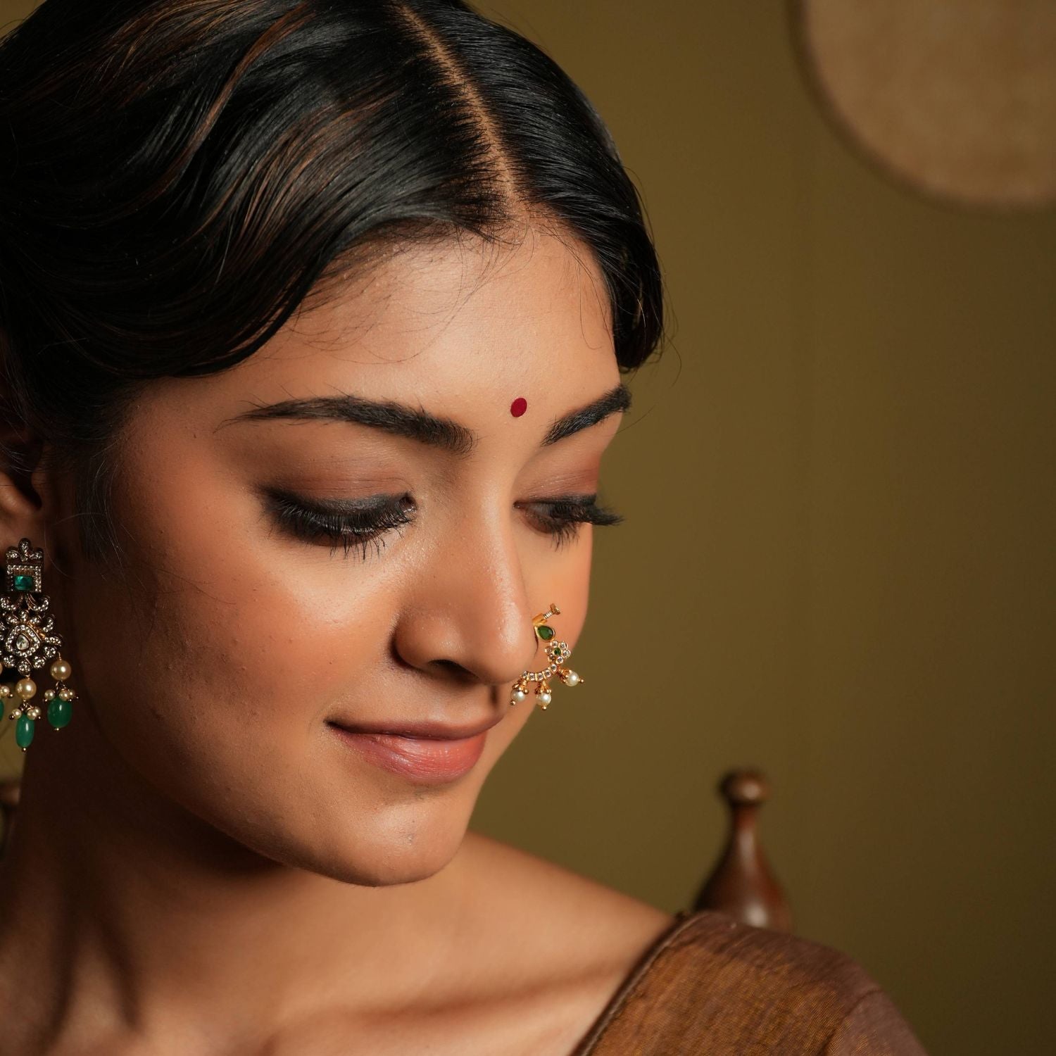 This gold plated silver nose ring shines with delicate
elegance, featuring a white Kundan setting and minimal stone set flower motif. Three bold
pearl edgings add a touch of luxurious sophistication, evoking the rich heritage of Indian
craftsmanship.