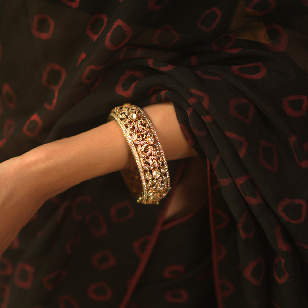A gold bangle with intricate filigree and royal carvings.