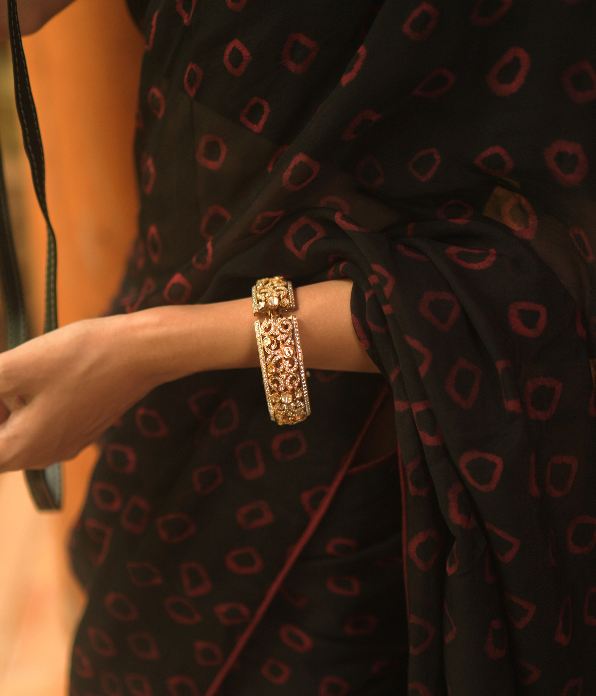 A gold bangle with intricate filigree and royal carvings.