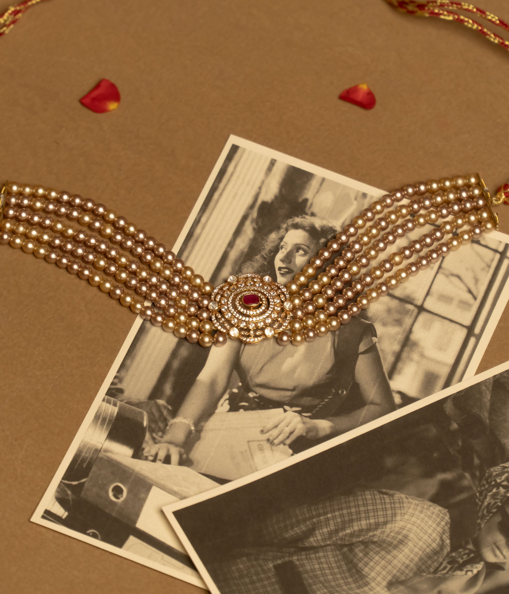 A gold choker featuring multiple strands of white pearls and a central sunburst-style medallion with red and white stones, worn on a person's neck.