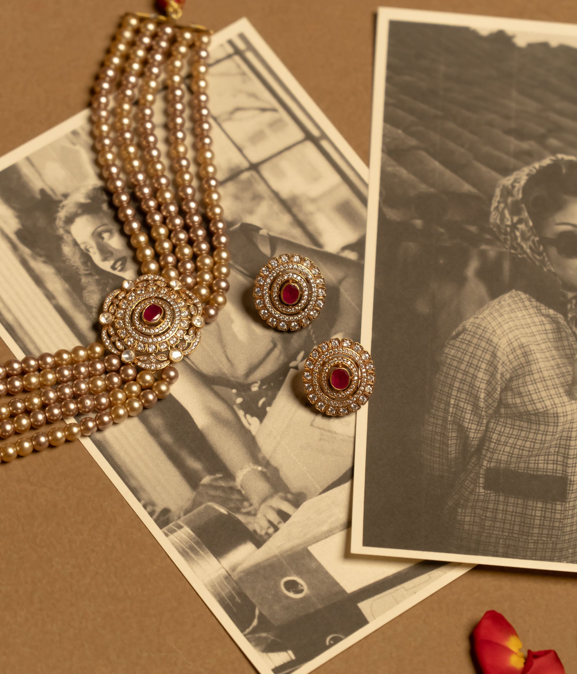A gold choker featuring multiple strands of white pearls and a central sunburst-style medallion with red and white stones, worn on a person's neck.