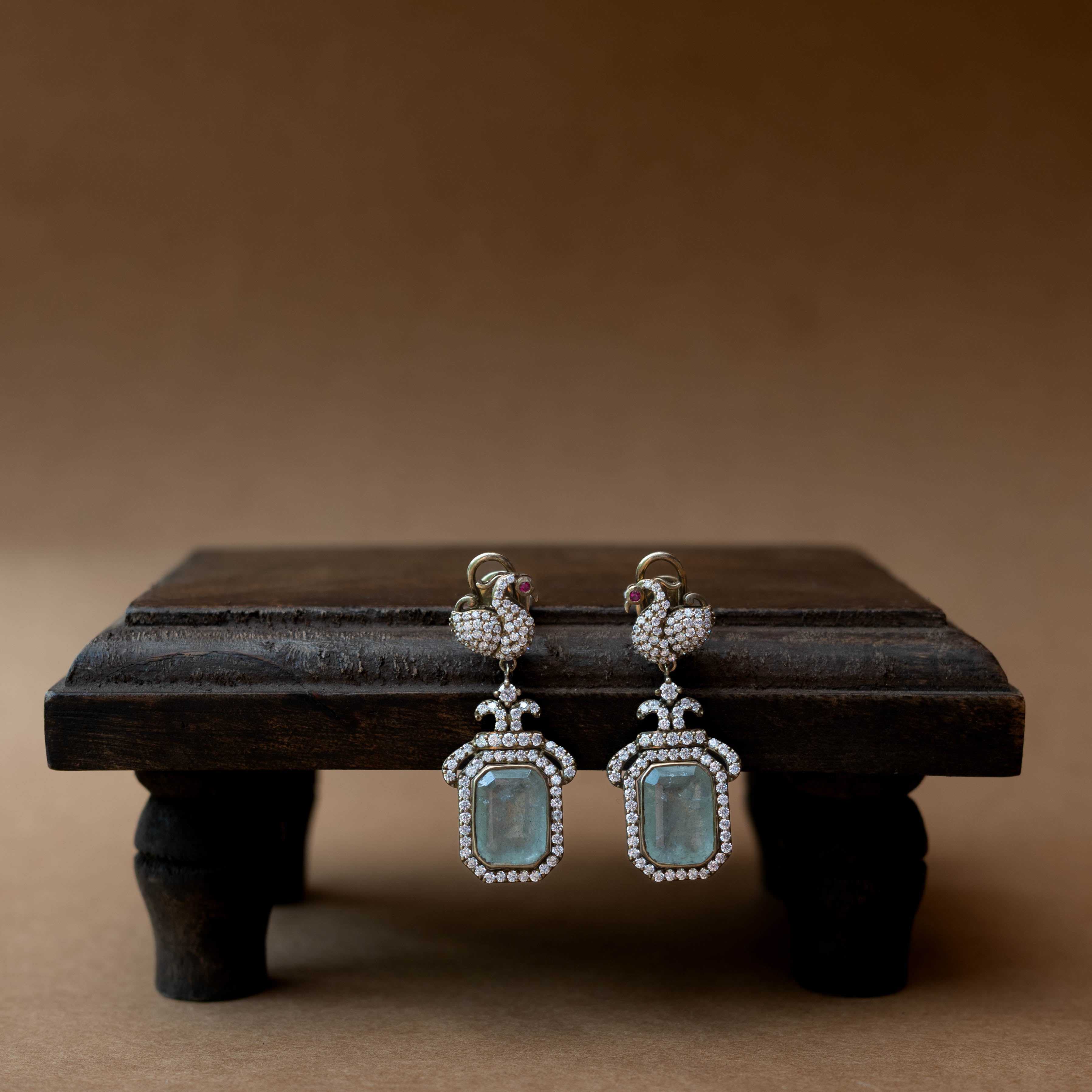 Intricate earrings with clear stones, a central red stone, and a dangling green stone.