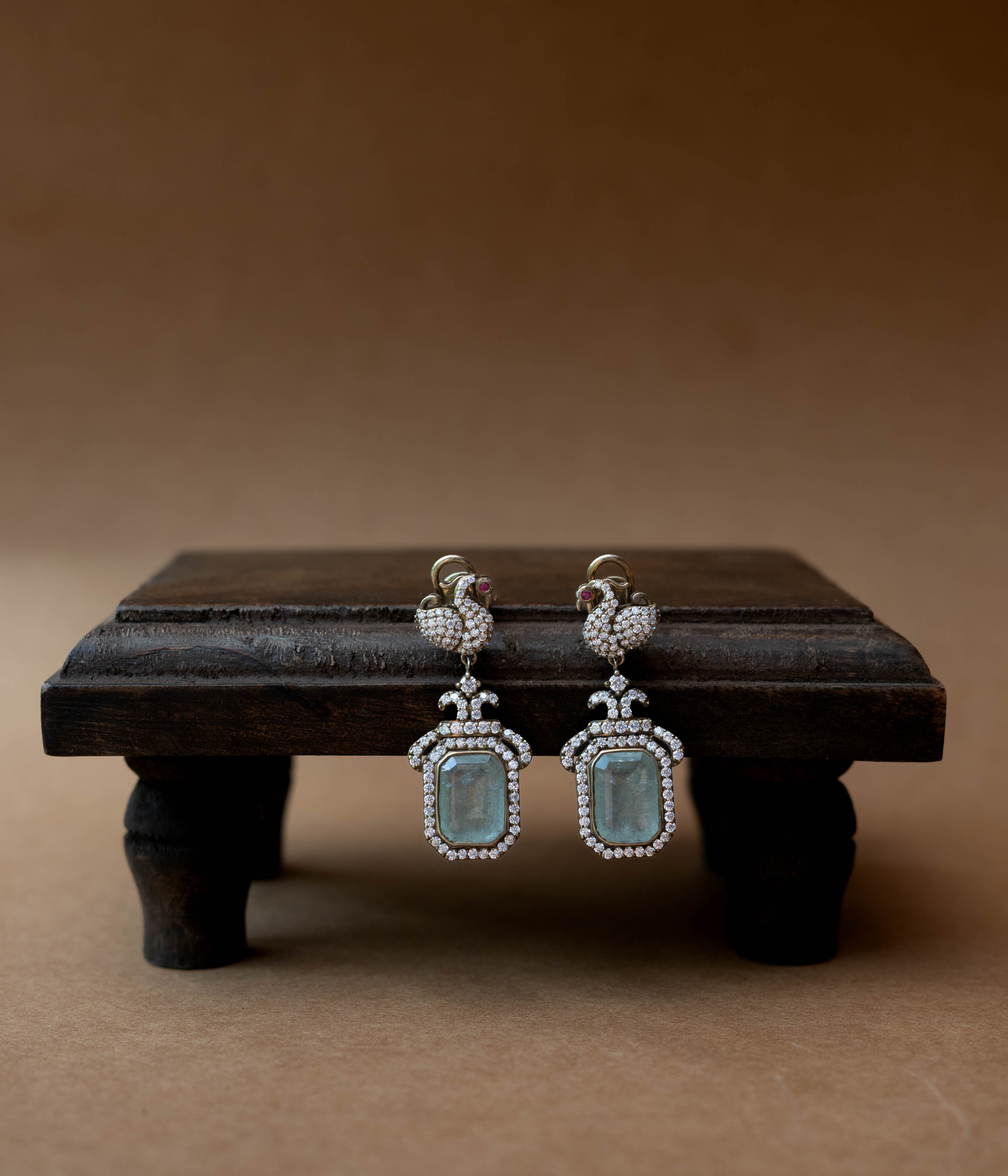 Intricate earrings with clear stones, a central red stone, and a dangling green stone.