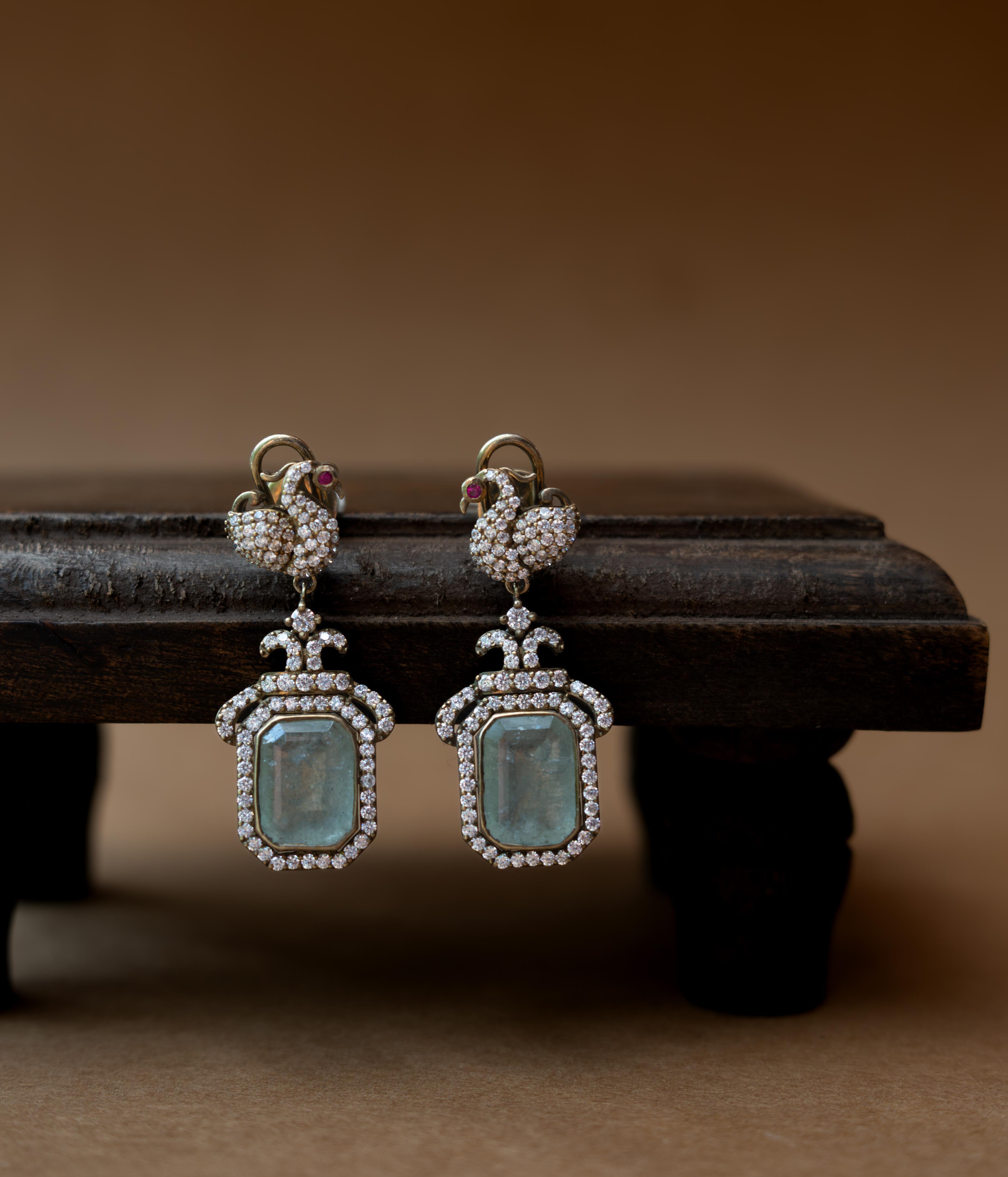 Intricate earrings with clear stones, a central red stone, and a dangling green stone.