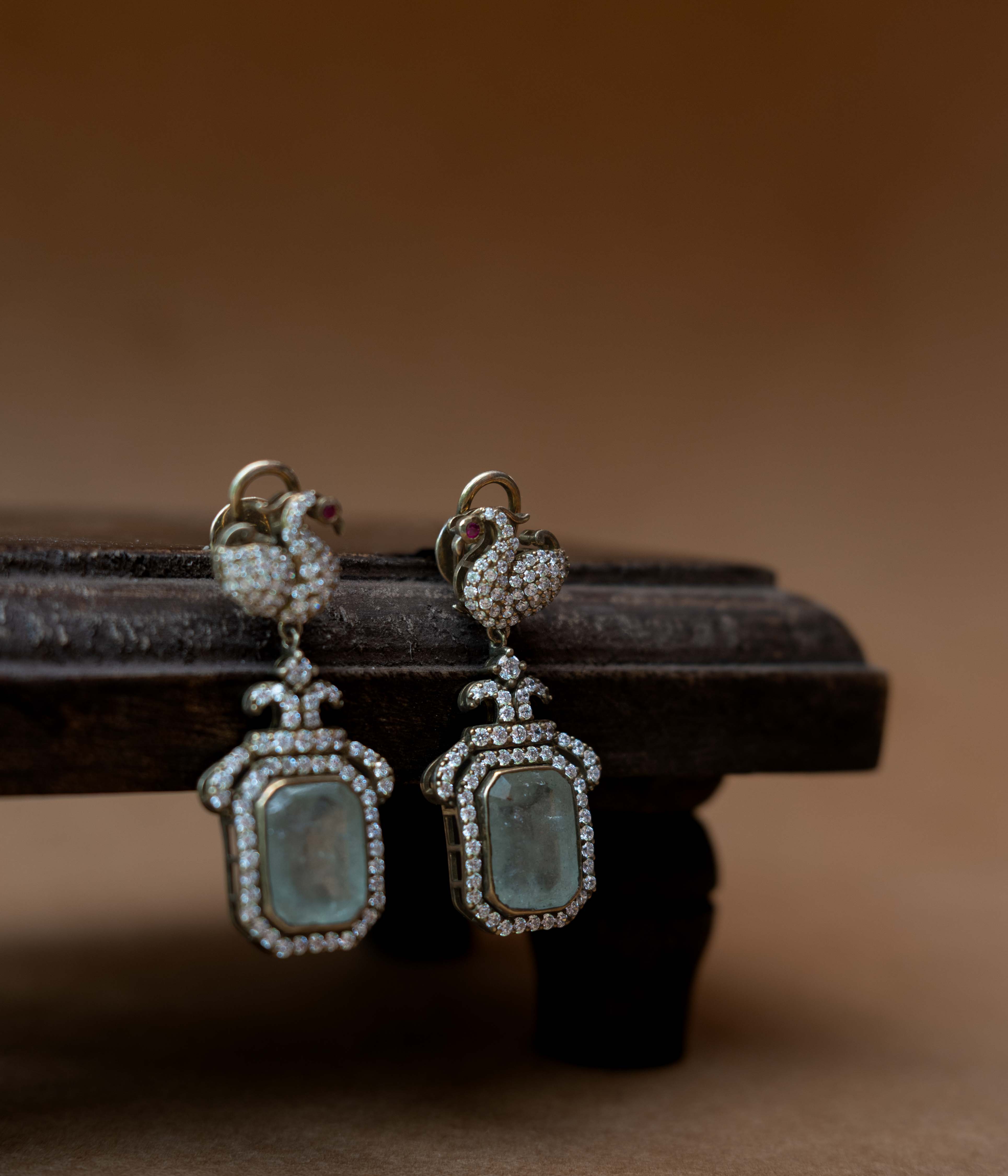 Intricate earrings with clear stones, a central red stone, and a dangling green stone.
