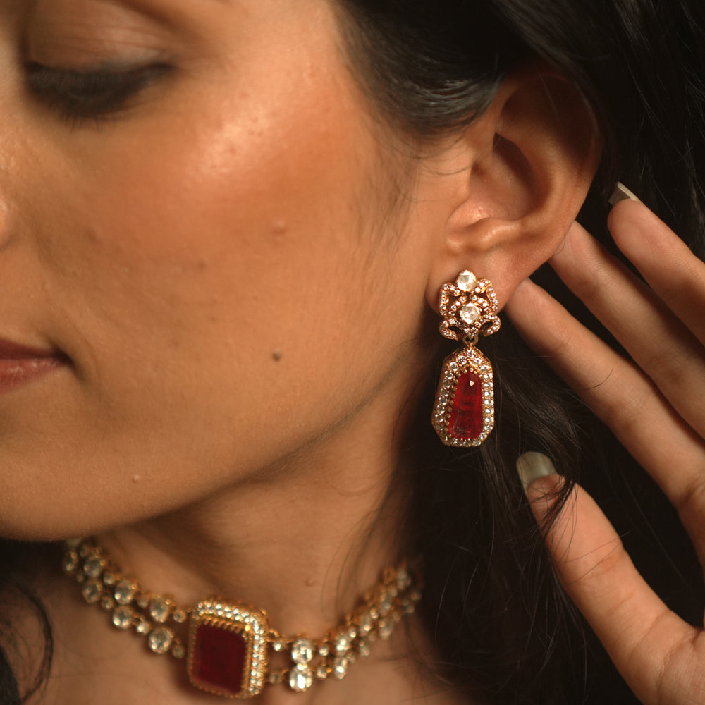 Gold earrings with a floral top, a large red stone, and a drop of white moissanite.