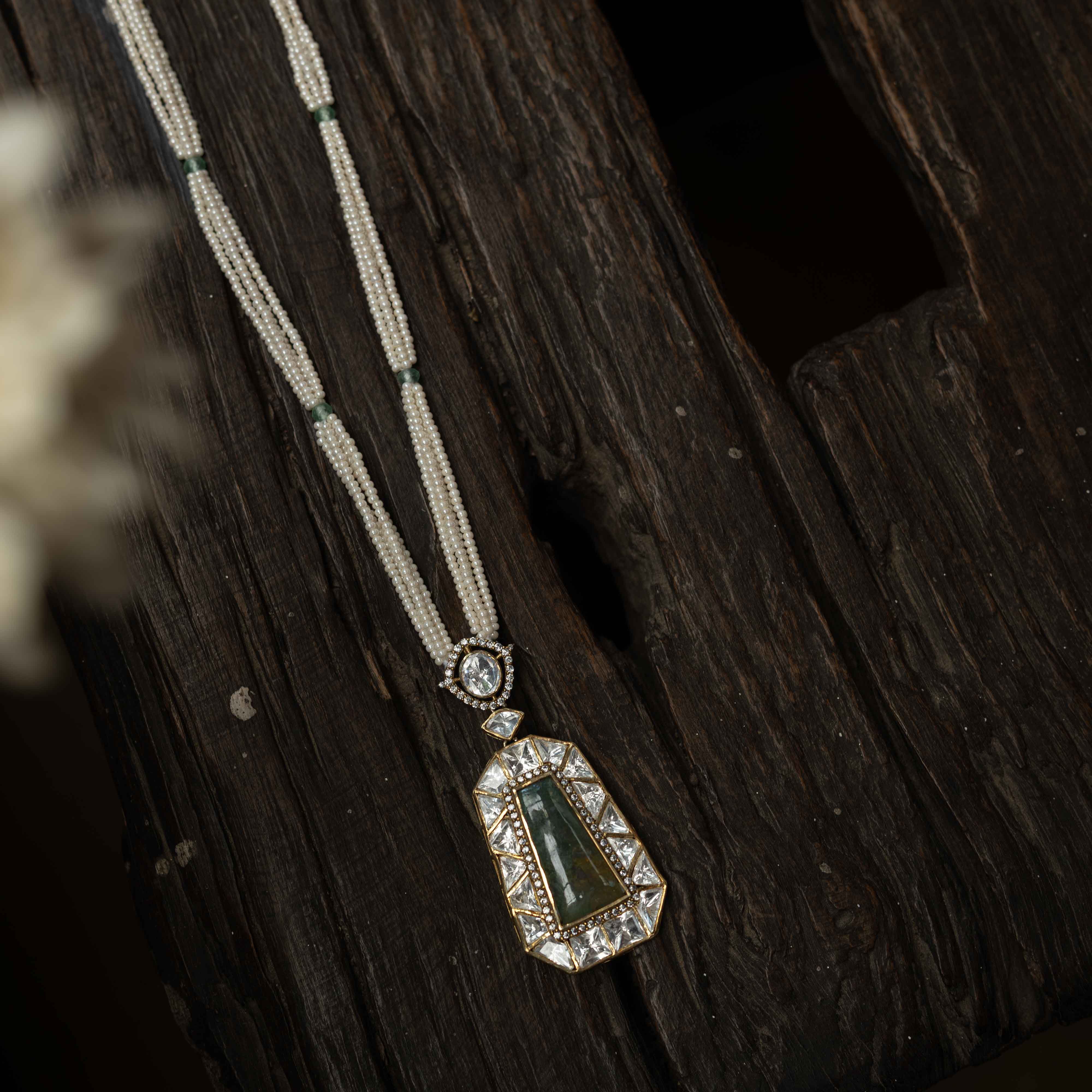 An intricate choker-style necklace with a green gem centerpiece, clear stones, and pearl drops.
