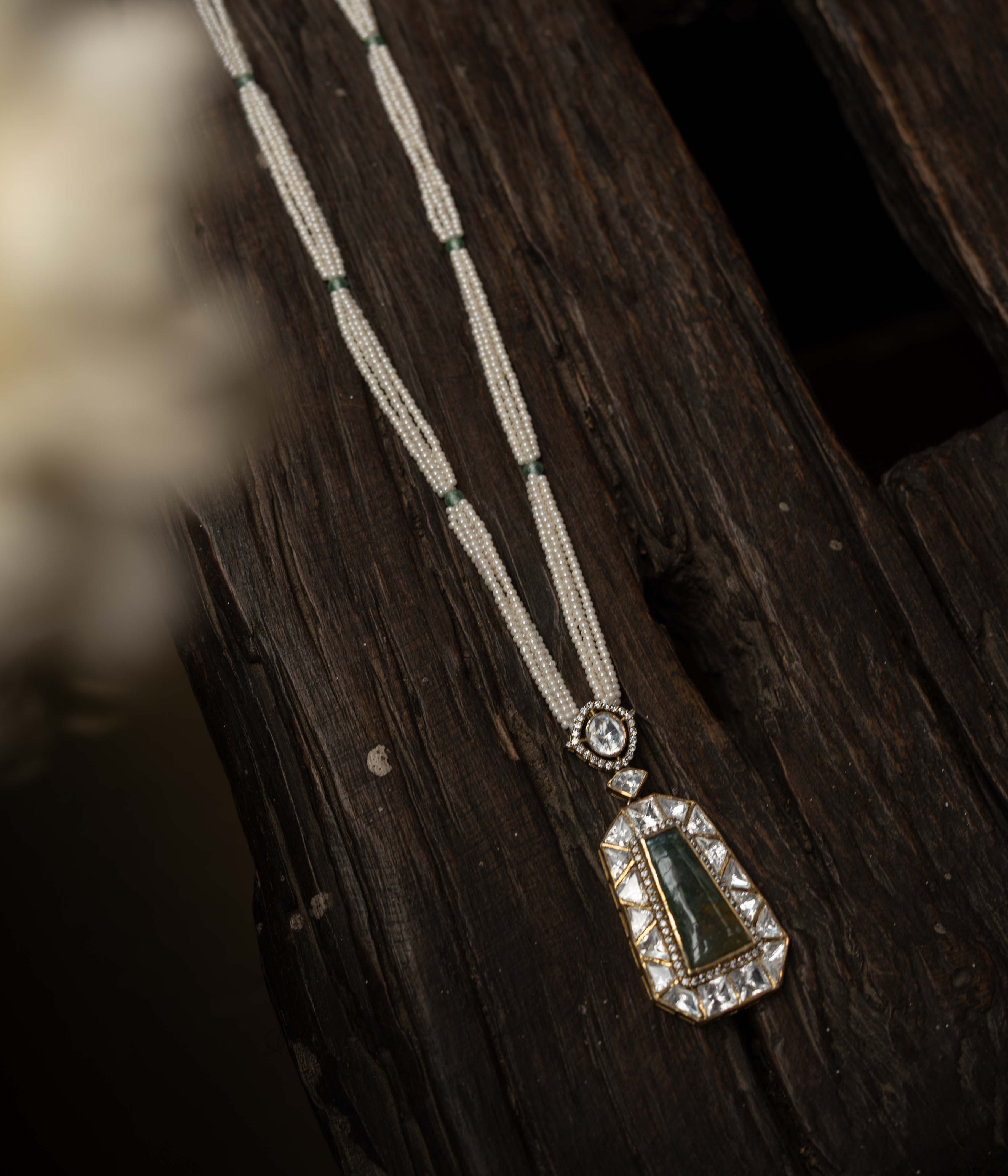 An intricate choker-style necklace with a green gem centerpiece, clear stones, and pearl drops.