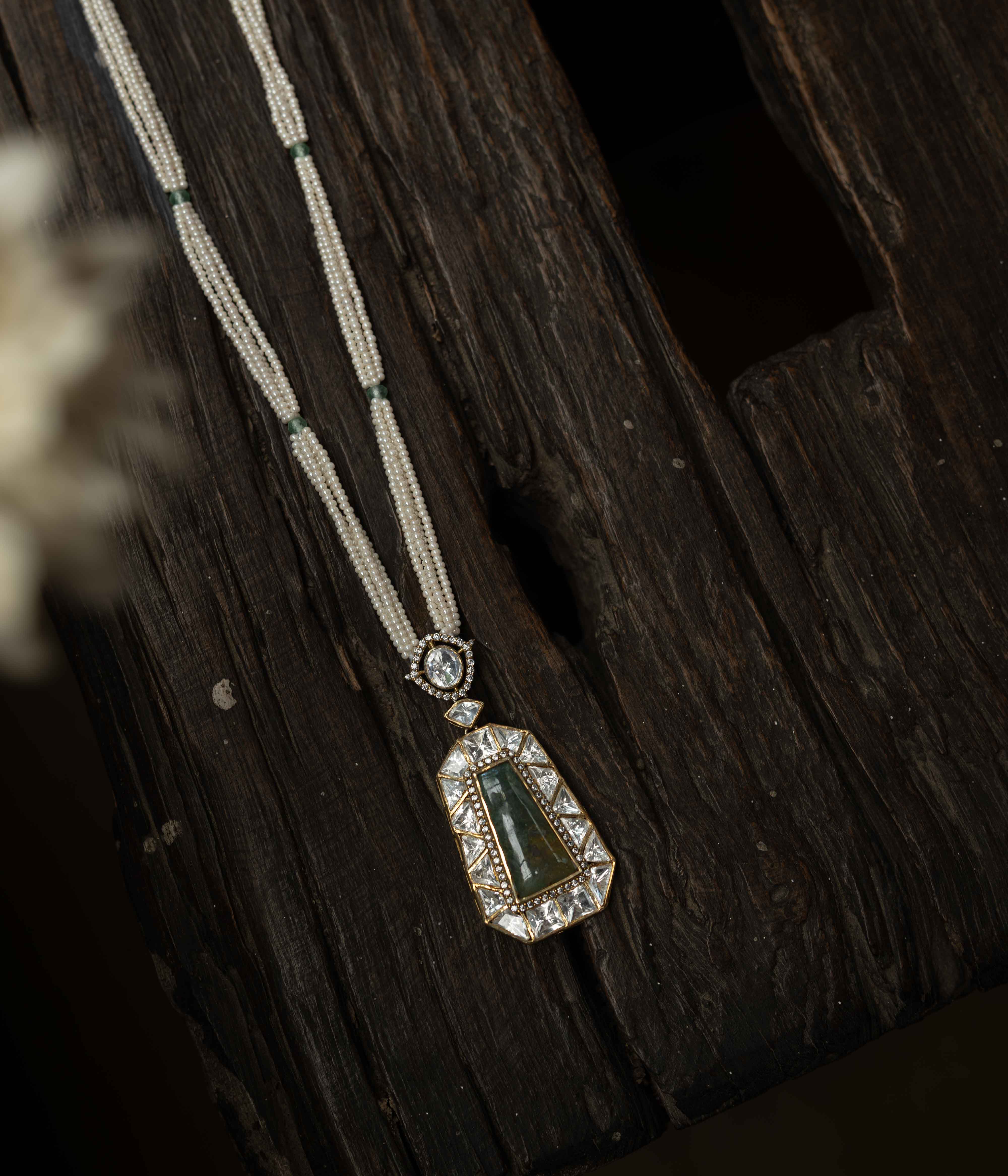 An intricate choker-style necklace with a green gem centerpiece, clear stones, and pearl drops.