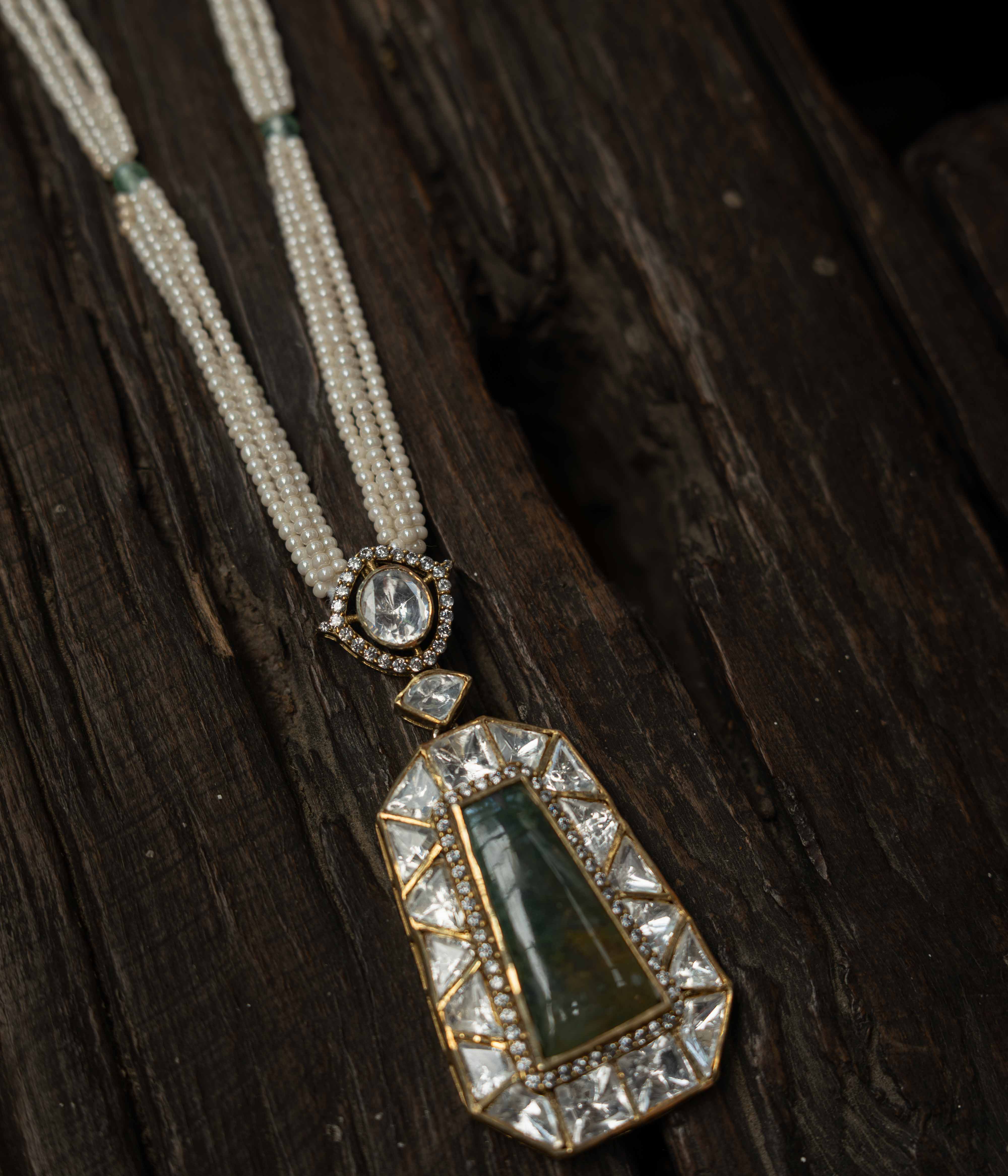 An intricate choker-style necklace with a green gem centerpiece, clear stones, and pearl drops.