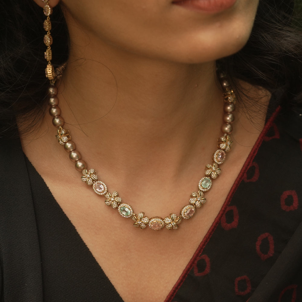 A necklace with multiple strands of pearls and three round, floral medallions with red and green stones.