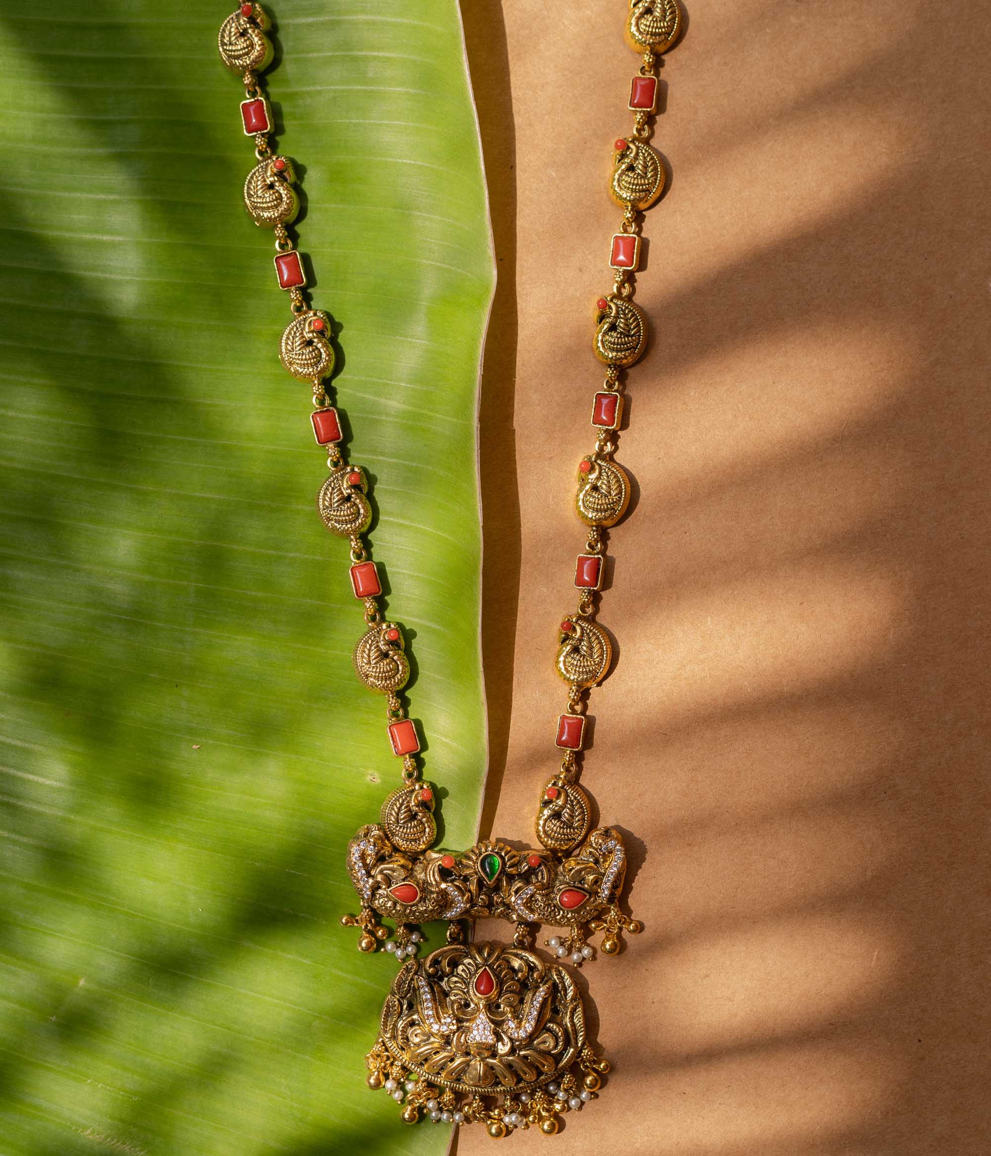 A 92.5 sterling silver Mythical Peacocks Antique Temple Necklace, likely gold-plated, featuring twin peacocks and a yali motif accented with red and green kempu stones, with a chain alternating between peacock links and coral-hued rectangular elements, a perfect heirloom-style piece for festive and bridal occasions.