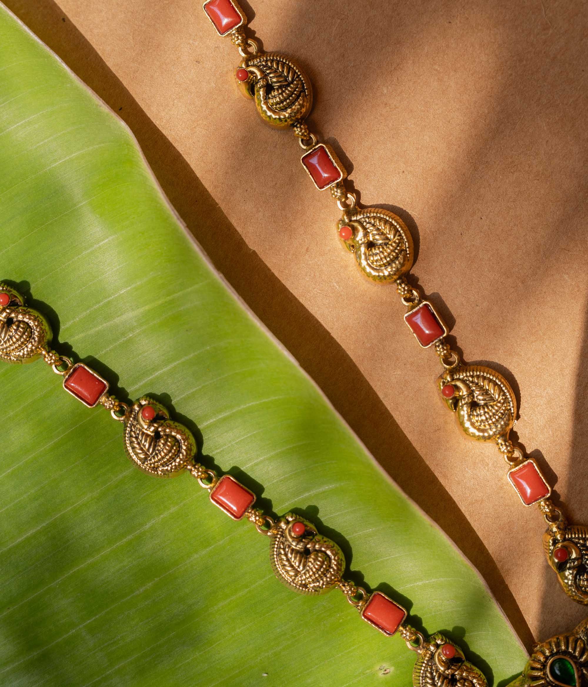 A 92.5 sterling silver Mythical Peacocks Antique Temple Necklace, likely gold-plated, featuring twin peacocks and a yali motif accented with red and green kempu stones, with a chain alternating between peacock links and coral-hued rectangular elements, a perfect heirloom-style piece for festive and bridal occasions.