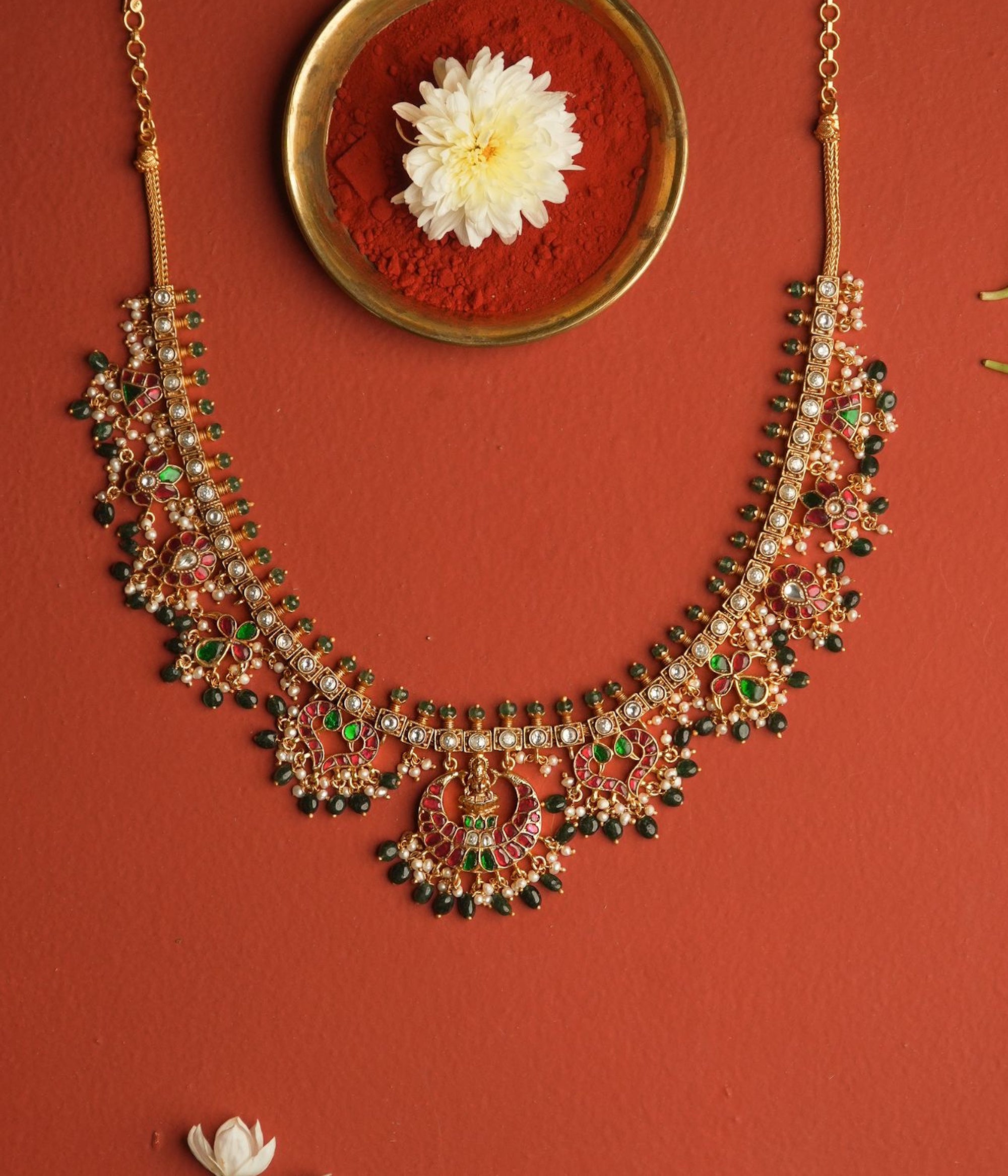 Ornate necklace with green and red stones on a red background