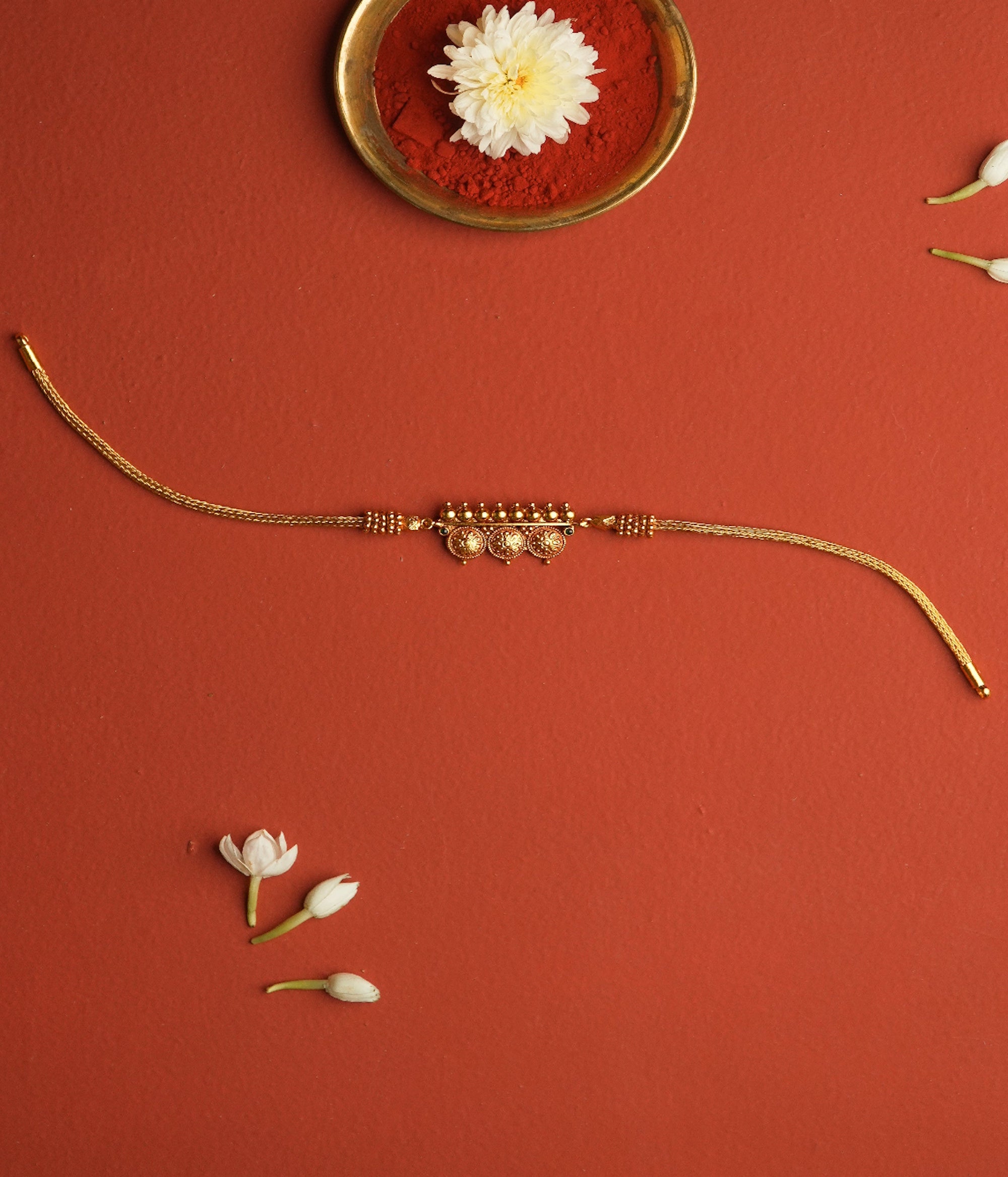Gold necklace on a red background with flowers and a small dish.